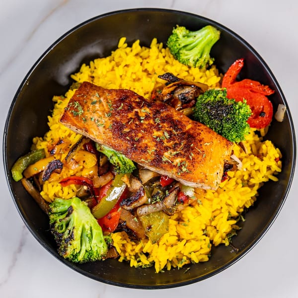 Grilled salmon with yellow rice, broccoli, and sautéed peppers in a black bowl.