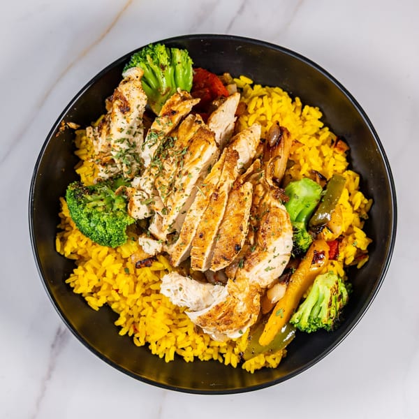 Grilled chicken slices, yellow rice, and roasted vegetables in a black bowl on a marble surface.