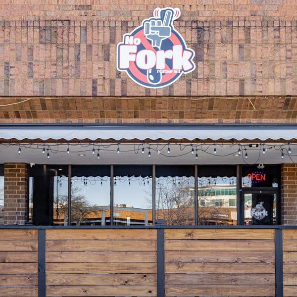 Exterior of No Fork Restaurant with its logo, awning, string lights, and wooden patio barrier.
