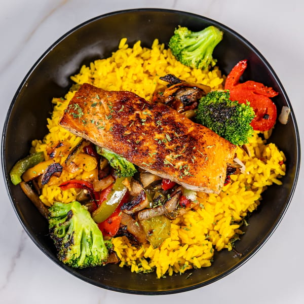 Grilled salmon with yellow rice, roasted broccoli, and bell peppers in a black bowl.