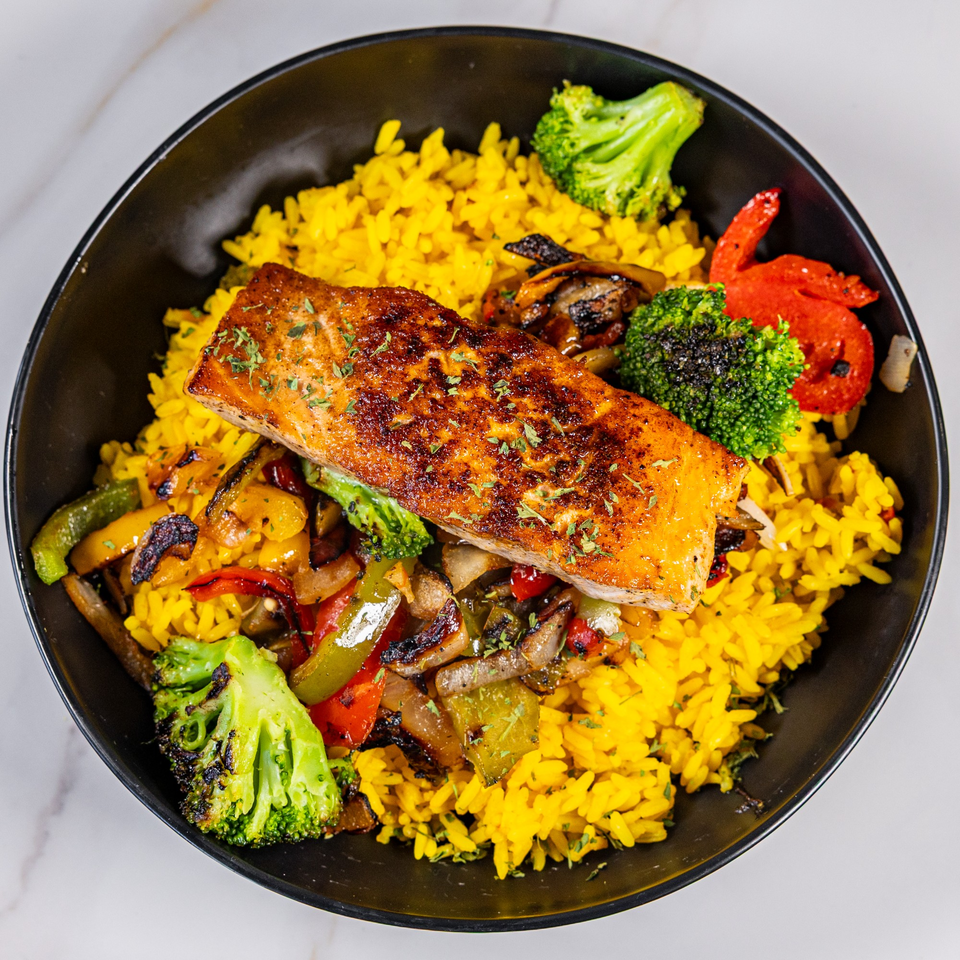 Grilled salmon with yellow rice, roasted broccoli, and bell peppers in a black bowl.