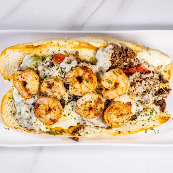 A shrimp and steak Philly cheesesteak sandwich, topped with melted cheese and parsley, on a white plate.