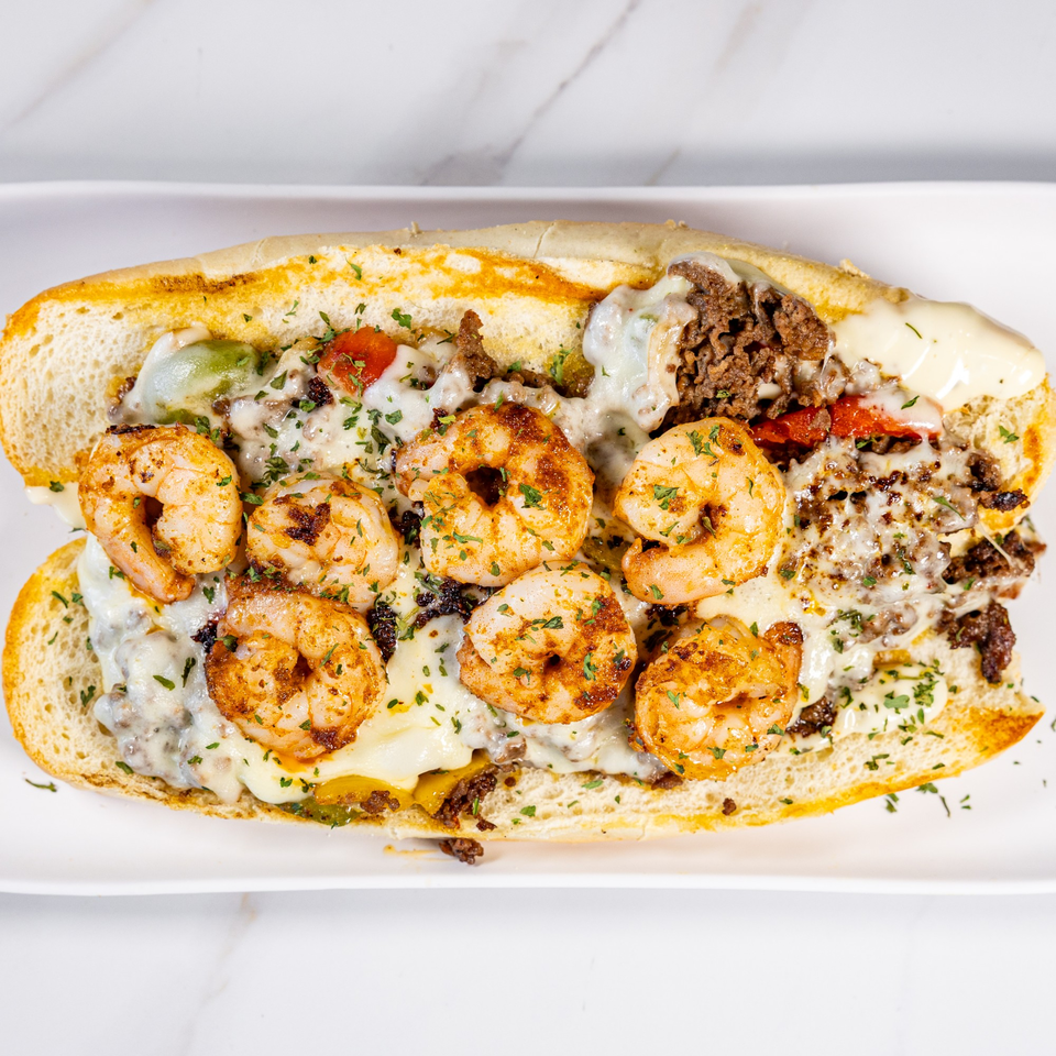 A shrimp and steak Philly cheesesteak sandwich, topped with melted cheese and parsley, on a white plate.