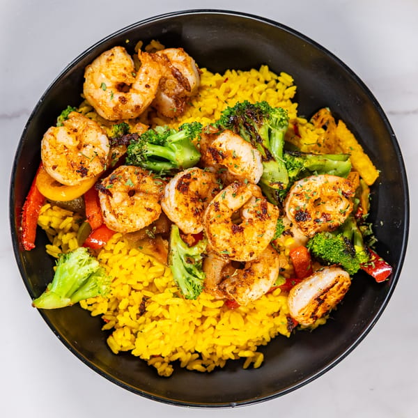 Grilled shrimp with yellow rice, broccoli, and bell peppers in a black bowl.