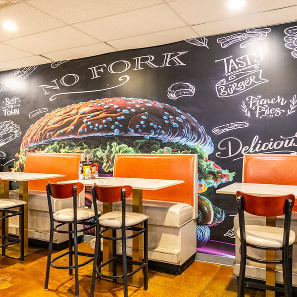 No Fork Restaurant interior with orange booths, high-top tables, and a large burger mural on the wall.