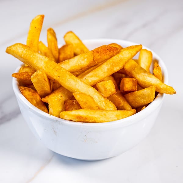 A white bowl filled with golden-brown french fries, lightly seasoned, on a white marble surface.