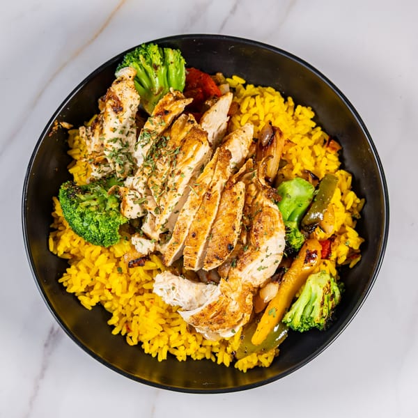 Grilled chicken slices with yellow rice, broccoli, and bell peppers in a black bowl.