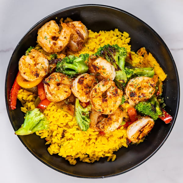 A black bowl filled with yellow rice, grilled shrimp, broccoli, and bell peppers.