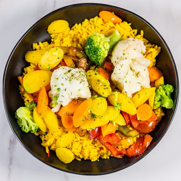 A black bowl filled with yellow rice, roasted vegetables, and herbs on a white marble surface.